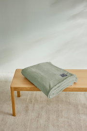 Gefaltete, hellgrüne Kuscheldecke von s.Oliver auf einem Holztisch, seitliche Perspektive.