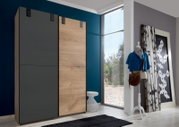 Moderner Schwebetürenschrank CARDIFF mit zwei Türen, eine in Holzoptik und die andere in dunklem Grau, in einem stilvollen Raum mit Blick auf den Schrank von vorne.