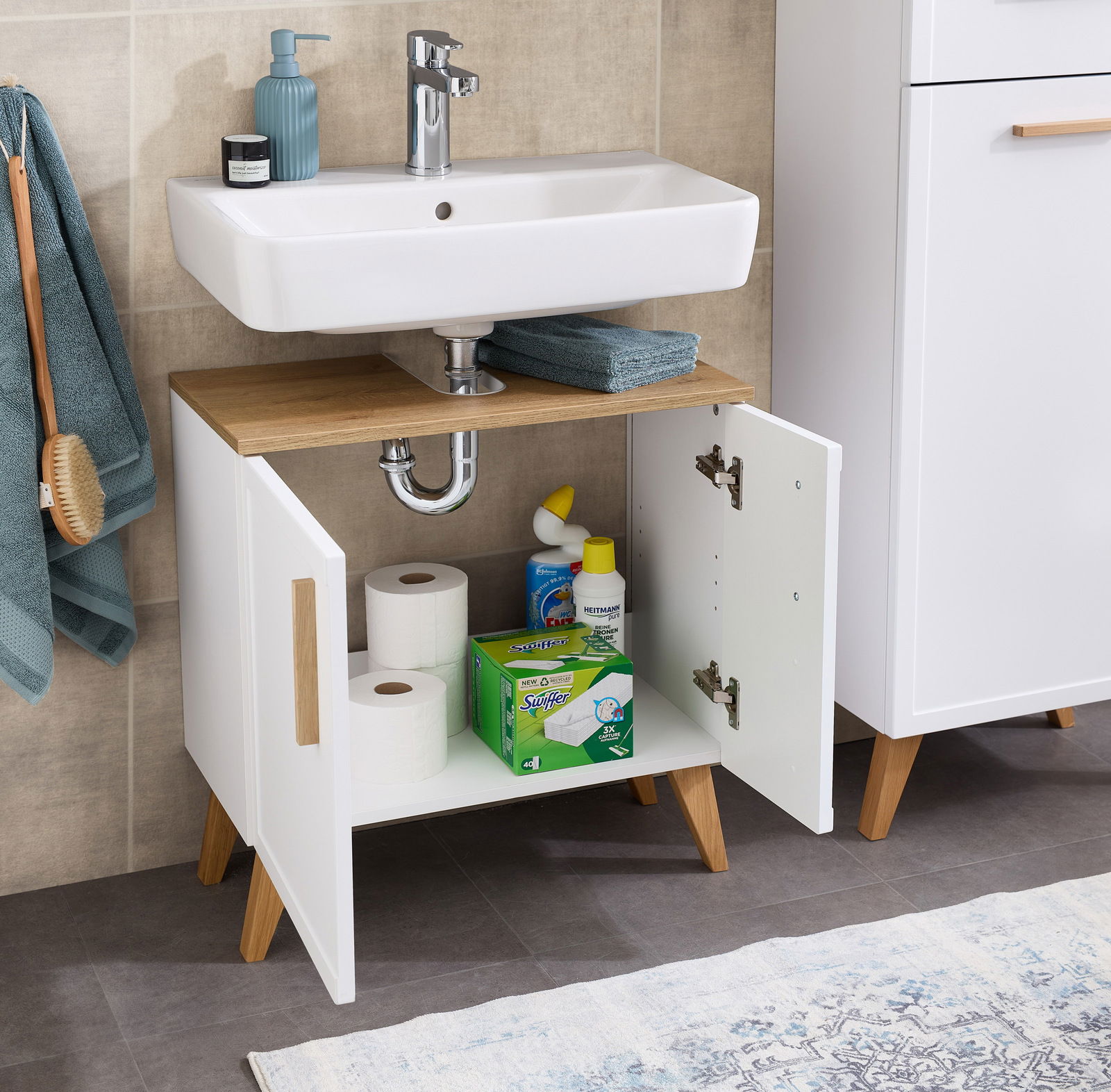 Waschbeckenunterschrank mit offenen Türen, gefüllt mit Reinigungsmitteln und Toilettenpapier, aus einer frontalen Perspektive fotografiert.