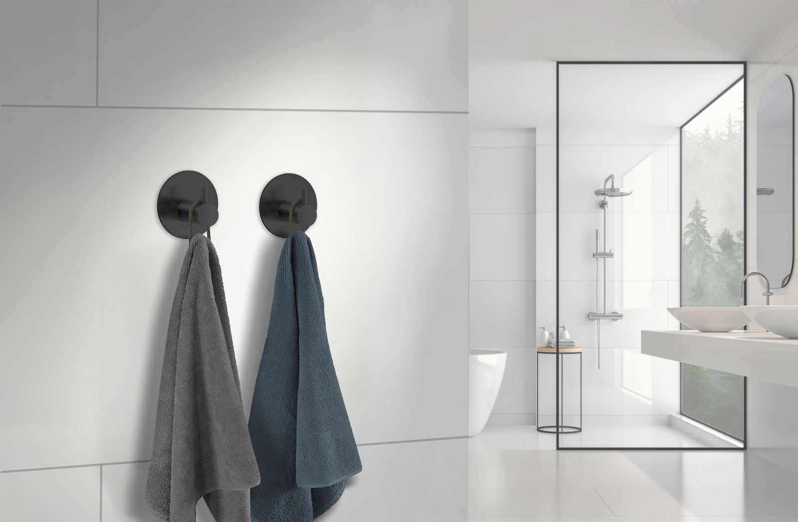 Zwei schwarze Edelstahlhaken an einer weißen Badezimmerwand, von denen jeweils ein Handtuch hängt. Die Perspektive zeigt die Haken von vorne in einem modernen Badezimmer.