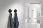 Zwei schwarze Edelstahlhaken an einer weißen Badezimmerwand, von denen jeweils ein Handtuch hängt. Die Perspektive zeigt die Haken von vorne in einem modernen Badezimmer.