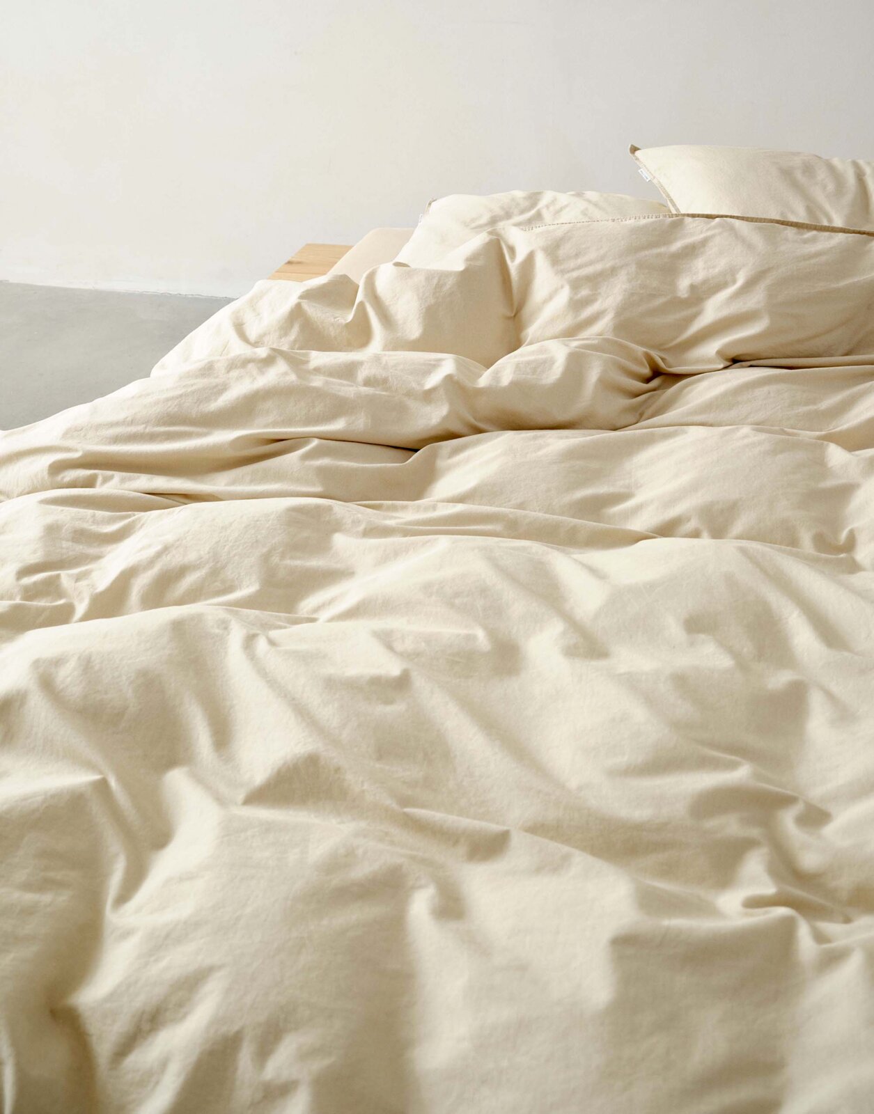 Beige Bettwäsche-Set auf einem Bett, fotografiert aus einer seitlichen Perspektive