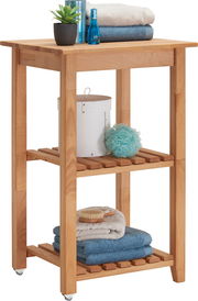 Holz-Servierwagen mit zwei Regalböden, dekoriert mit Handtüchern, Pflanzen und Pflegeartikeln, seitliche Perspektive
