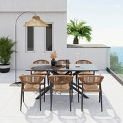 Moderner Stapelsessel aus Rattan mit schwarzem Metallgestell, auf einer Terrasse mit Meerblick und Palmen im Hintergrund, aus der Perspektive von vorne.