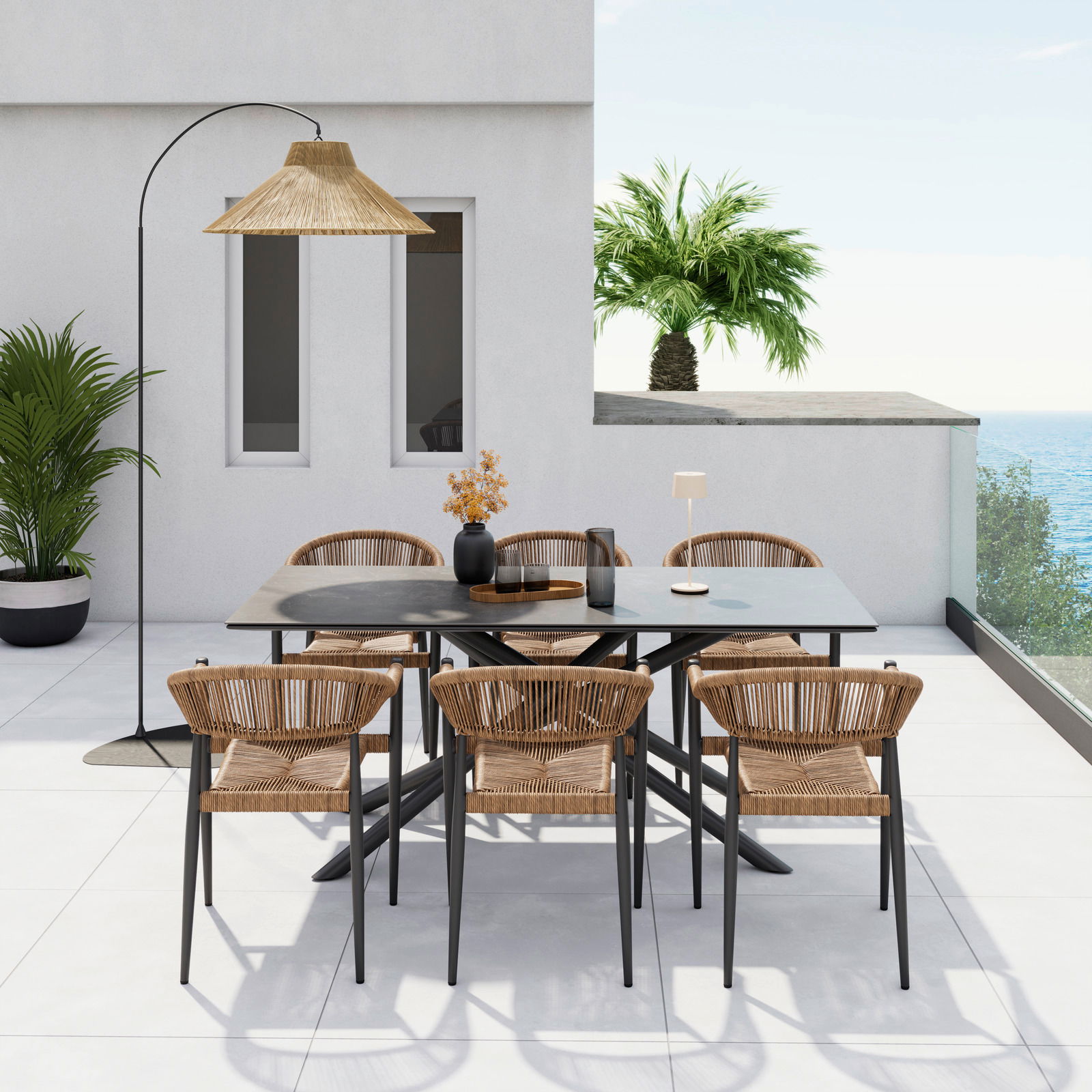 Moderner Stapelsessel aus Rattan mit schwarzem Metallgestell, auf einer Terrasse mit Meerblick und Palmen im Hintergrund, aus der Perspektive von vorne.