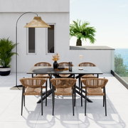 Moderne stapelstoel van rotan met een zwart metalen frame, op een terras met uitzicht op zee en palmbomen op de achtergrond, gezien van voren.