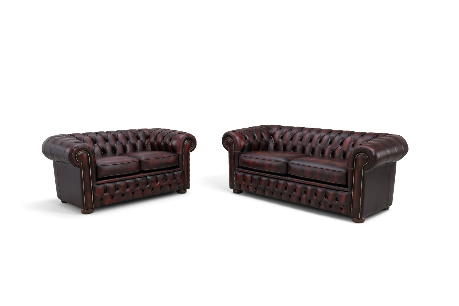 Zwei Chesterfield Sofas in dunklem Leder, frontal fotografiert, mit charakteristischer Knopfheftung und abgerundeten Armlehnen.