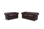 Zwei Chesterfield Sofas in dunklem Leder, frontal fotografiert, mit charakteristischer Knopfheftung und abgerundeten Armlehnen.