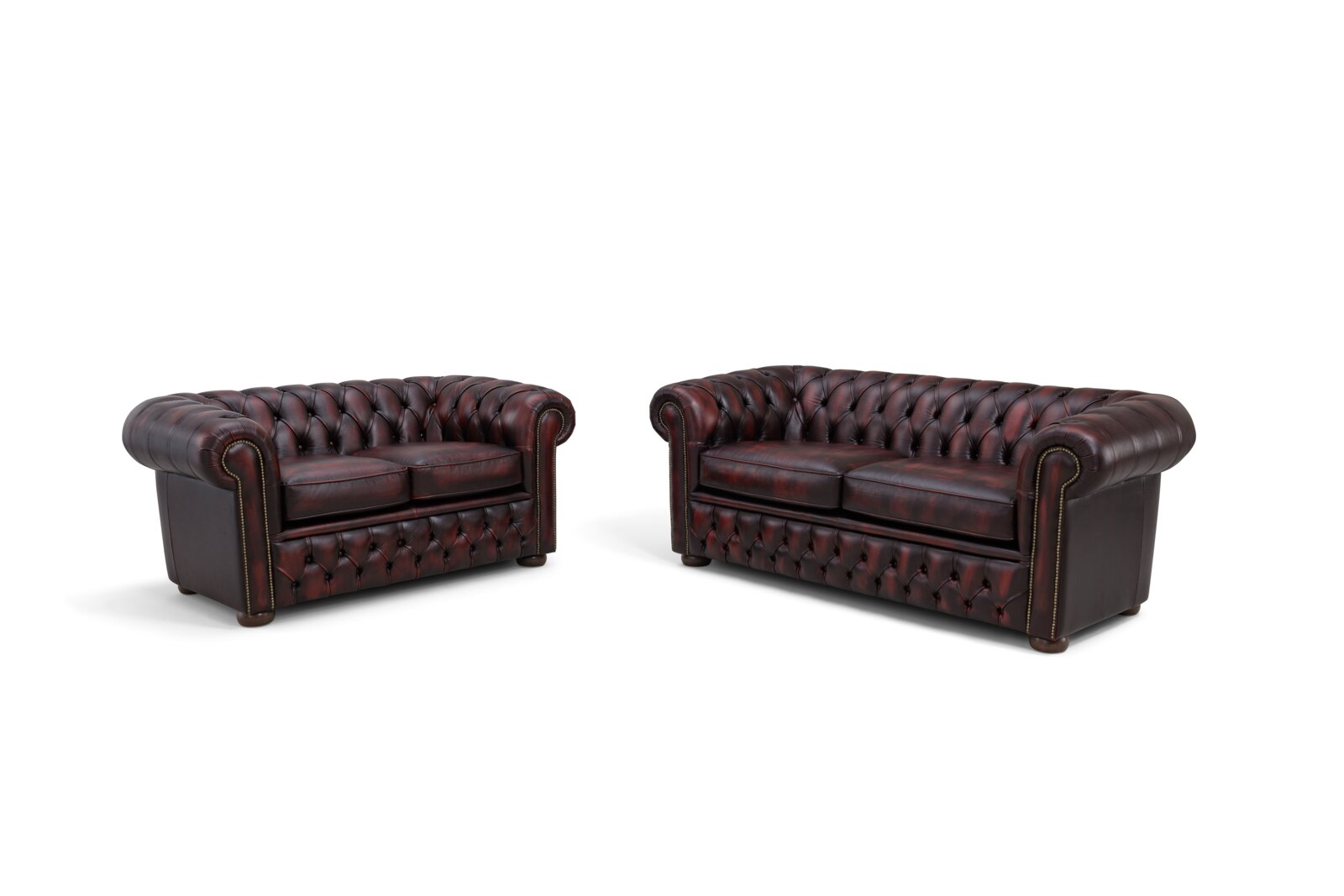 Twee Chesterfield-banken van donker leer, van voren gefotografeerd, met de kenmerkende knopenbekleding en afgeronde armleuningen.