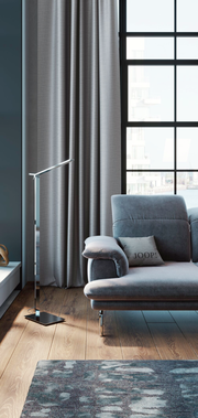 Grauer Ösenvorhang in einem modernen Wohnzimmer mit Blick auf ein großes Fenster und ein graues Sofa. Perspektive von der Seite.