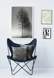 Zwei dekorative Kissenhüllen mit geometrischem Muster in einem blauen Stuhl, umgeben von minimalistischen Wandbildern. Frontalansicht.