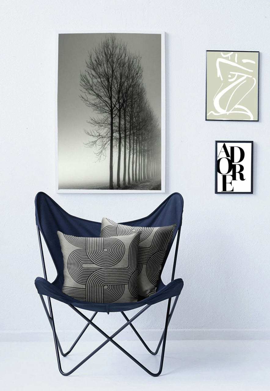 Zwei dekorative Kissenhüllen mit geometrischem Muster in einem blauen Stuhl, umgeben von minimalistischen Wandbildern. Frontalansicht.