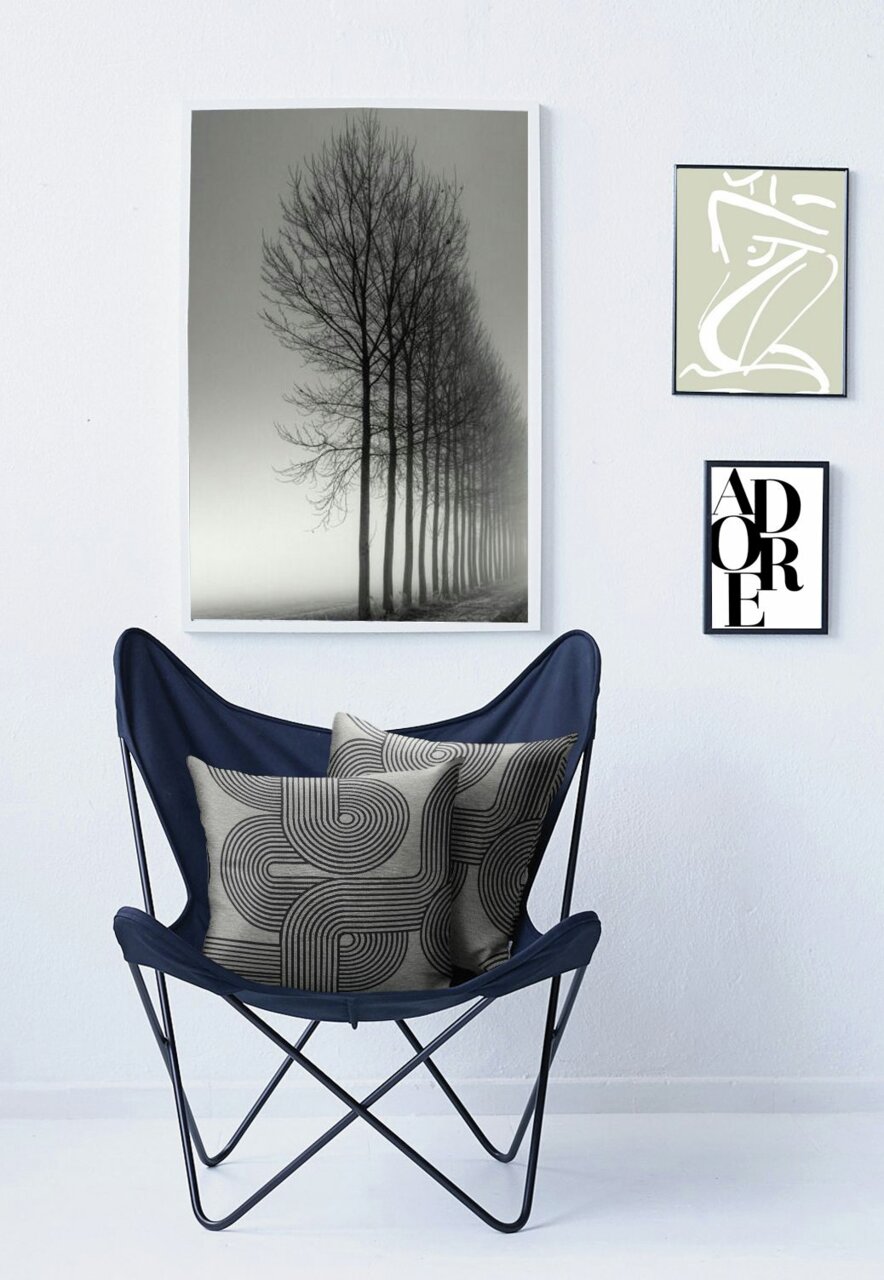 Zwei dekorative Kissenhüllen mit geometrischem Muster in einem blauen Stuhl, umgeben von minimalistischen Wandbildern. Frontalansicht.