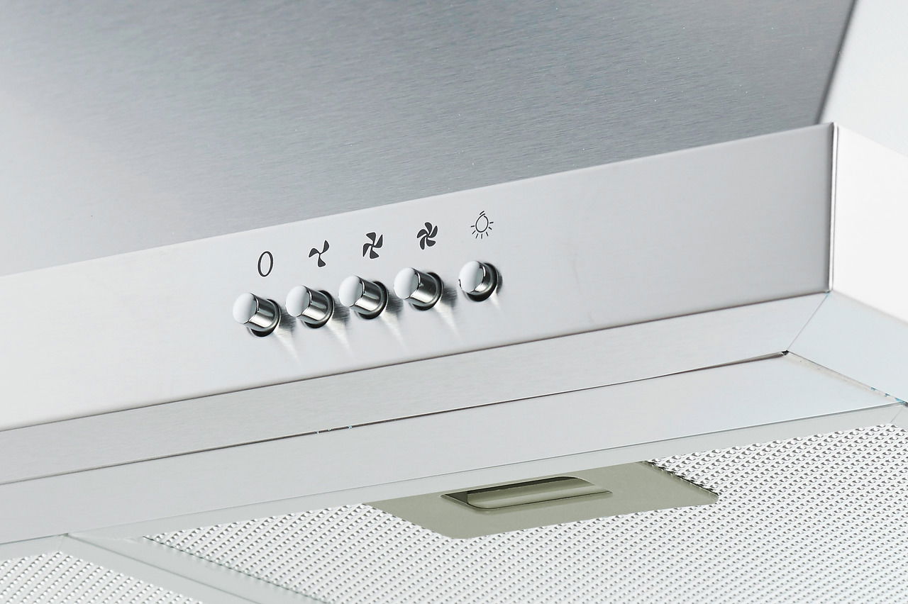Nahaufnahme einer modernen Edelstahl-Dunstabzugshaube mit Bedienknöpfen und Lüftungsgitter, von unten betrachtet.