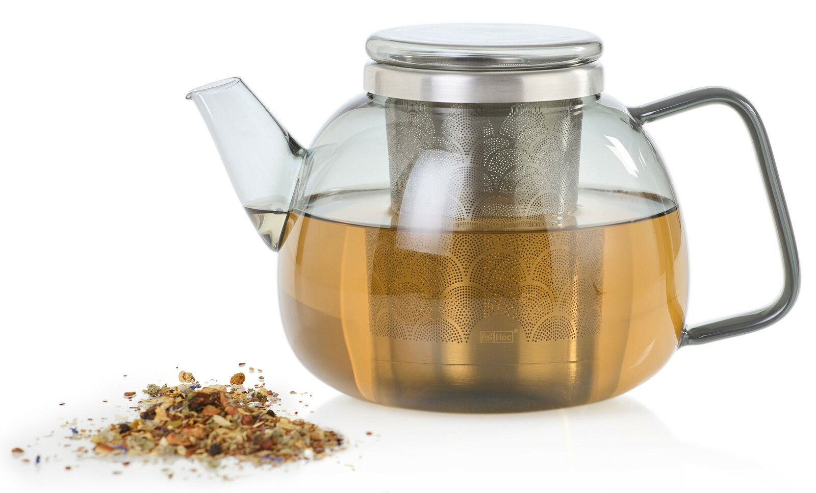 Glas-Teekanne Yuna mit Edelstahl-Filter, seitliche Perspektive, gefüllt mit Tee, daneben lose Teeblätter.