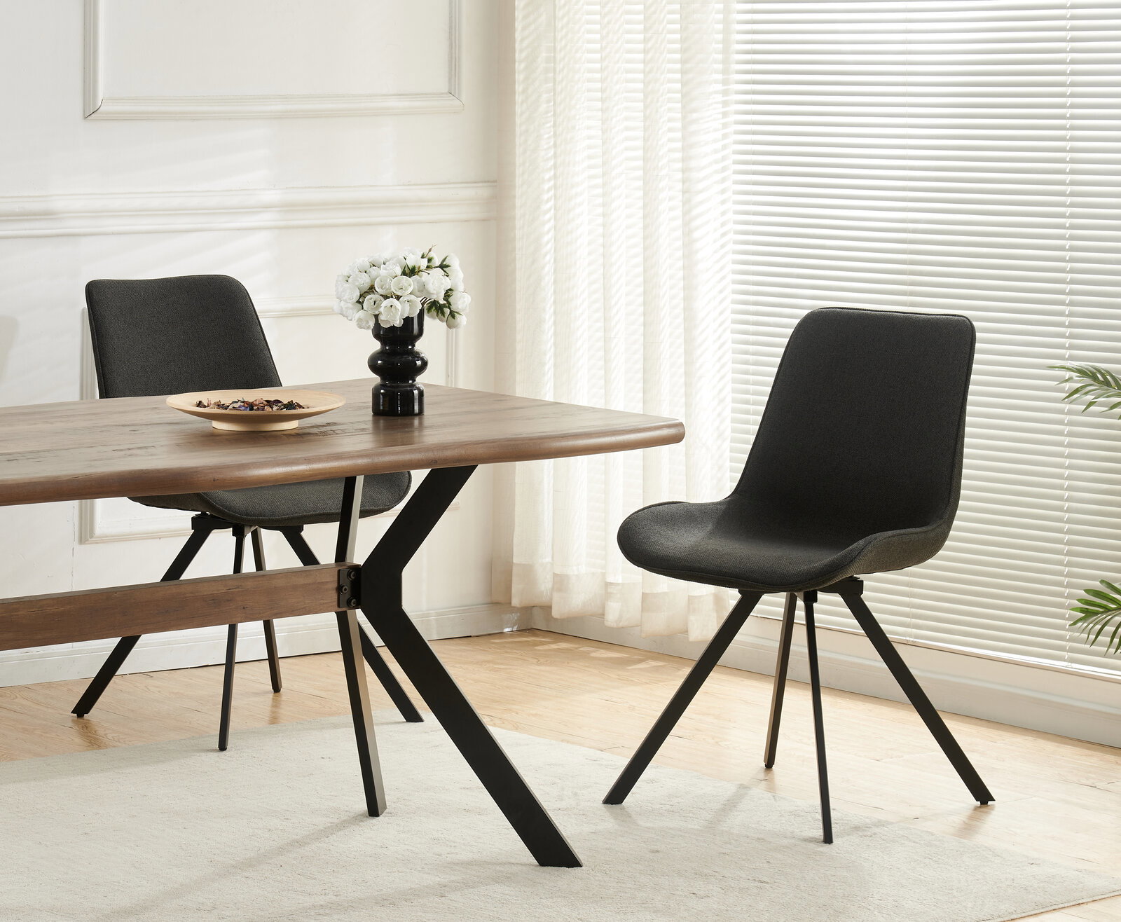 Moderner Esszimmerstuhl in Dunkelgrau mit gepolsterter Sitzschale und schwarzen Metallbeinen neben Holzesstisch, seitliche Perspektive im hellen Wohnraum
