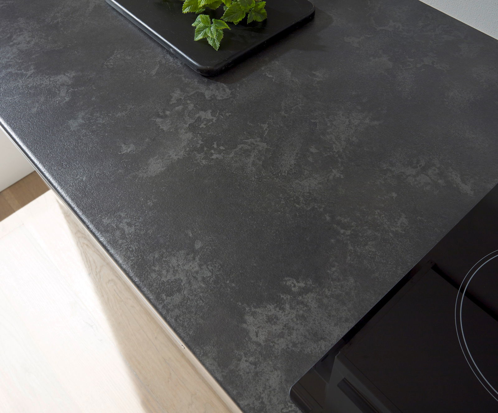 Draufsicht auf eine moderne, dunkle Küchenarbeitsplatte mit glatter Oberfläche und einem Teil eines Kochfelds.