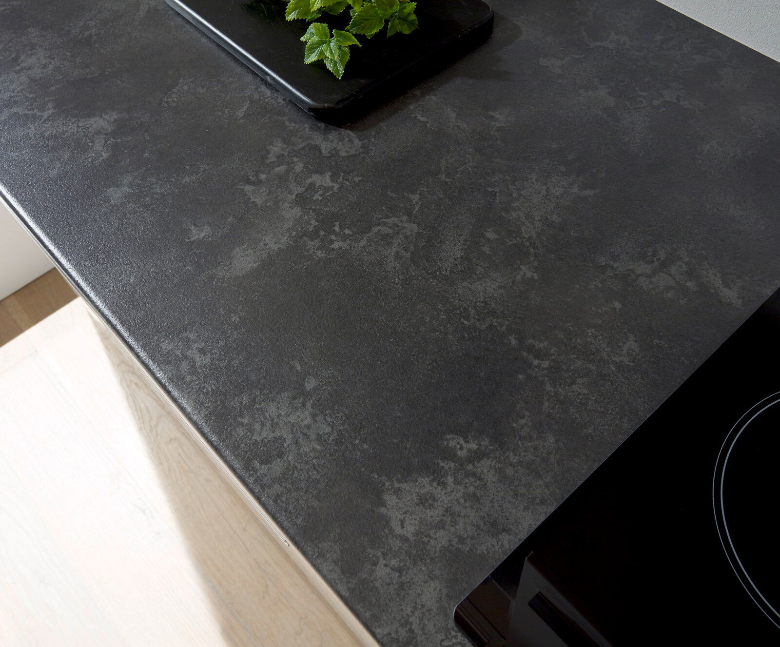 Draufsicht auf eine moderne, dunkle Küchenarbeitsplatte mit glatter Oberfläche und einem Teil eines Kochfelds.