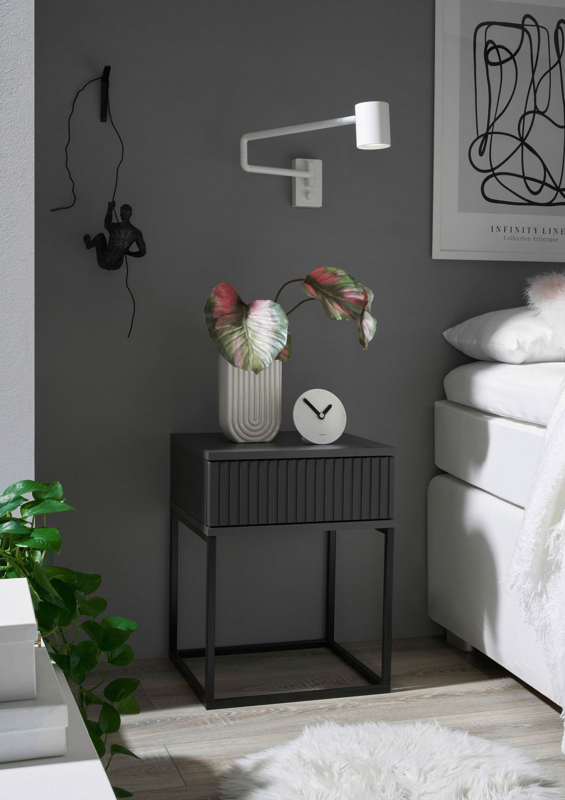 Moderne Nachtkommode in dunklem Design mit dekorativer Pflanze und Uhr, seitliche Perspektive
