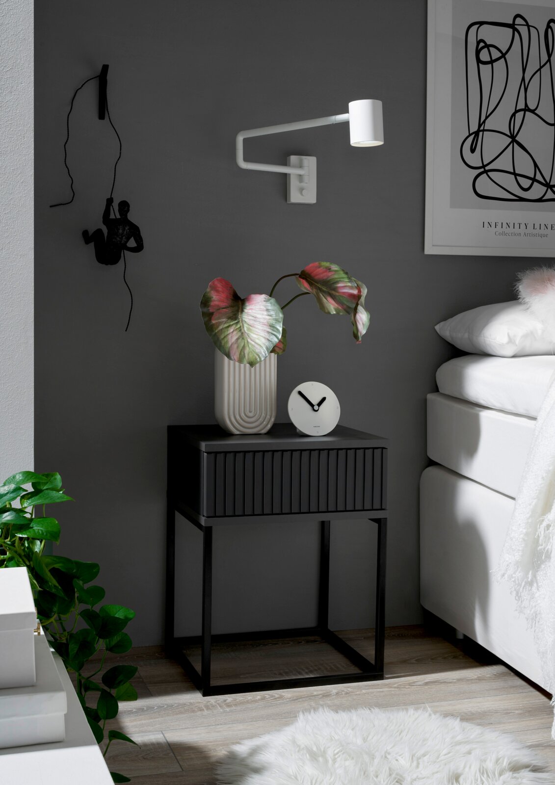 Moderne Nachtkommode in dunklem Design mit dekorativer Pflanze und Uhr, seitliche Perspektive