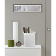 Weiße, schmale Aufbewahrungsbox mit perforiertem Design, gefüllt mit Büchern, auf einem weißen Möbelstück stehend, aus frontaler Perspektive.