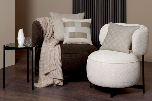 Zwei moderne Sessel mit stilvollen Zierkissen in einem eleganten Wohnzimmer-Setup, seitliche Perspektive.