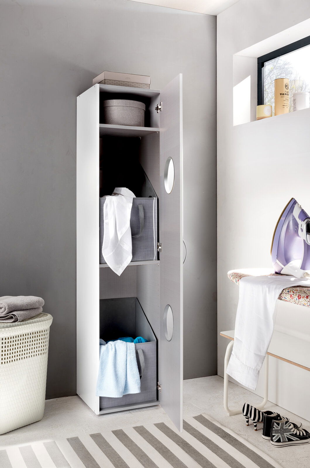 Moderner Wäscheschrank mit geöffneter Tür, gefüllt mit Wäschekörben und Handtüchern, aus seitlicher Perspektive fotografiert.