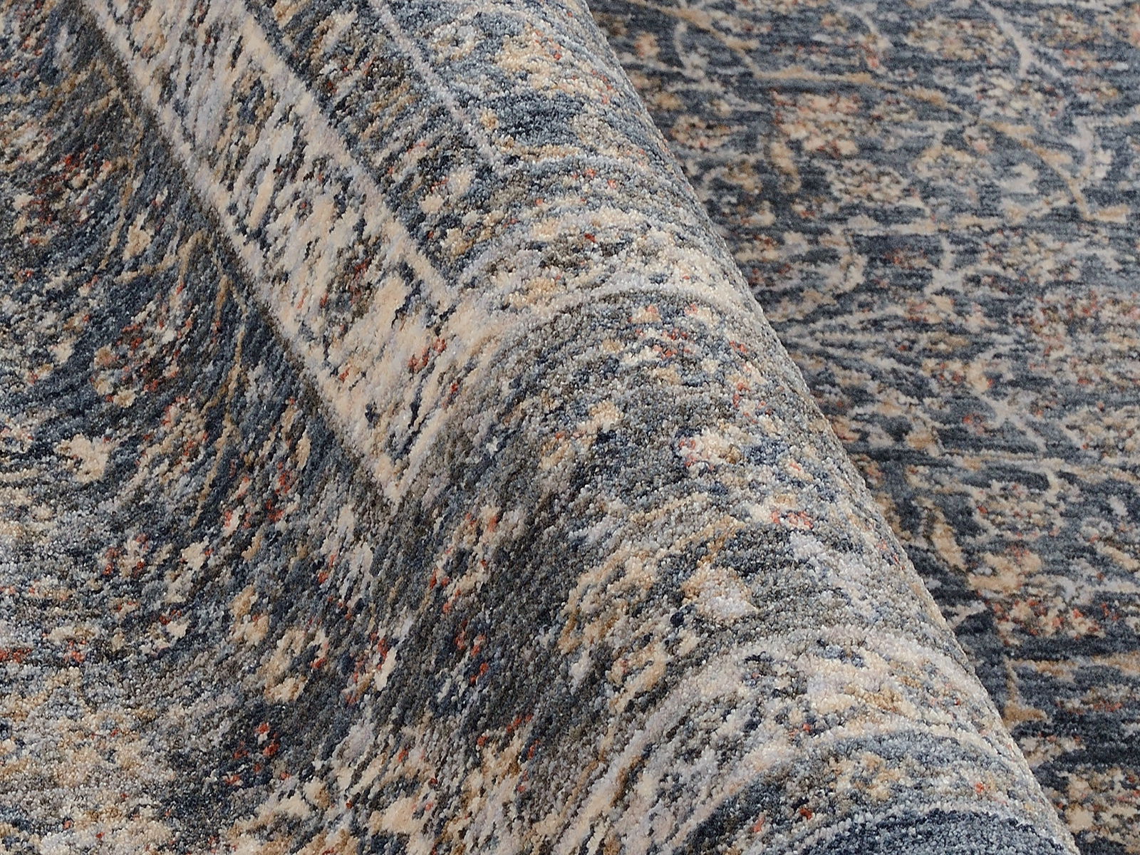 Nahaufnahme eines Frisé-Teppichs mit detailliertem Muster in Blau- und Beigetönen, seitliche Perspektive.
