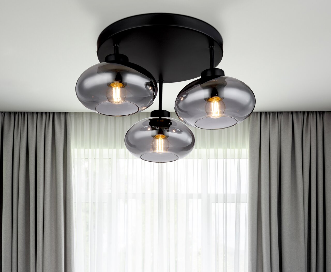 Globo Lighting Deckenleuchte SHAUN Moderne Deckenleuchte mit drei rauchgrauen Glaskugeln, von unten fotografiert, vor einem Fenster mit Vorhängen.