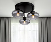 Moderne Deckenleuchte mit drei rauchgrauen Glaskugeln, von unten fotografiert, vor einem Fenster mit Vorhängen.