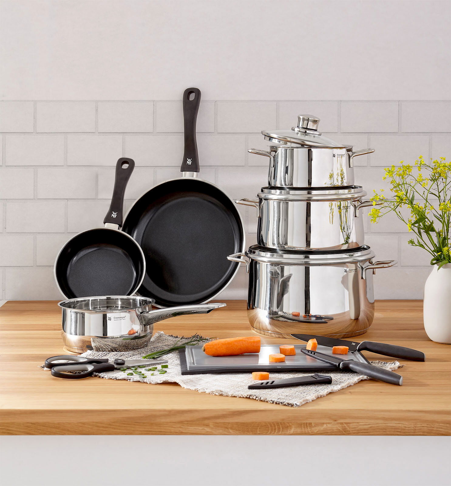 Kochtopf-Starter-Set 10-tlg. aus Edelstahl mit Töpfen, Pfannen und Küchenutensilien auf einer Holzarbeitsplatte, seitliche Perspektive.