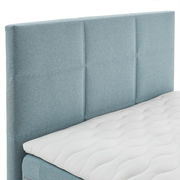 Boxspringbett mit hellblauem Kopfteil und weißer Matratze, seitliche Perspektive