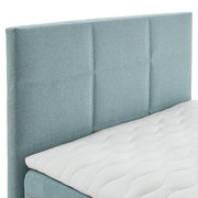 Boxspringbett mit hellblauem Kopfteil und weißer Matratze, seitliche Perspektive