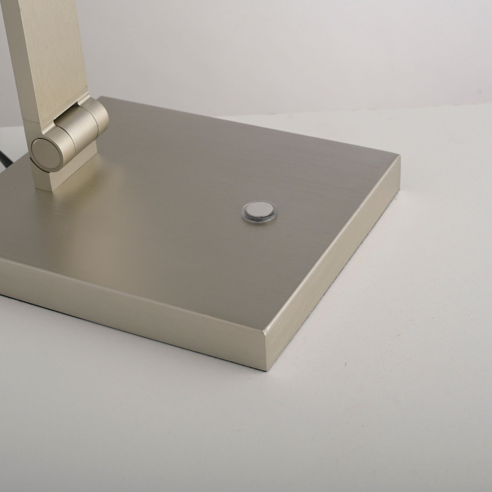 Nahaufnahme der Basis einer LED-Tischleuchte mit modernem, gebürstetem Metallfinish und einem runden Schalter, seitliche Perspektive.