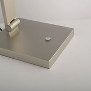 Nahaufnahme der Basis einer LED-Tischleuchte mit modernem, gebürstetem Metallfinish und einem runden Schalter, seitliche Perspektive.