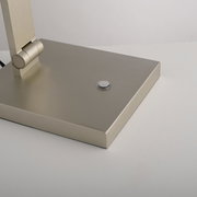 Nahaufnahme der Basis einer LED-Tischleuchte mit modernem, gebürstetem Metallfinish und einem runden Schalter, seitliche Perspektive.