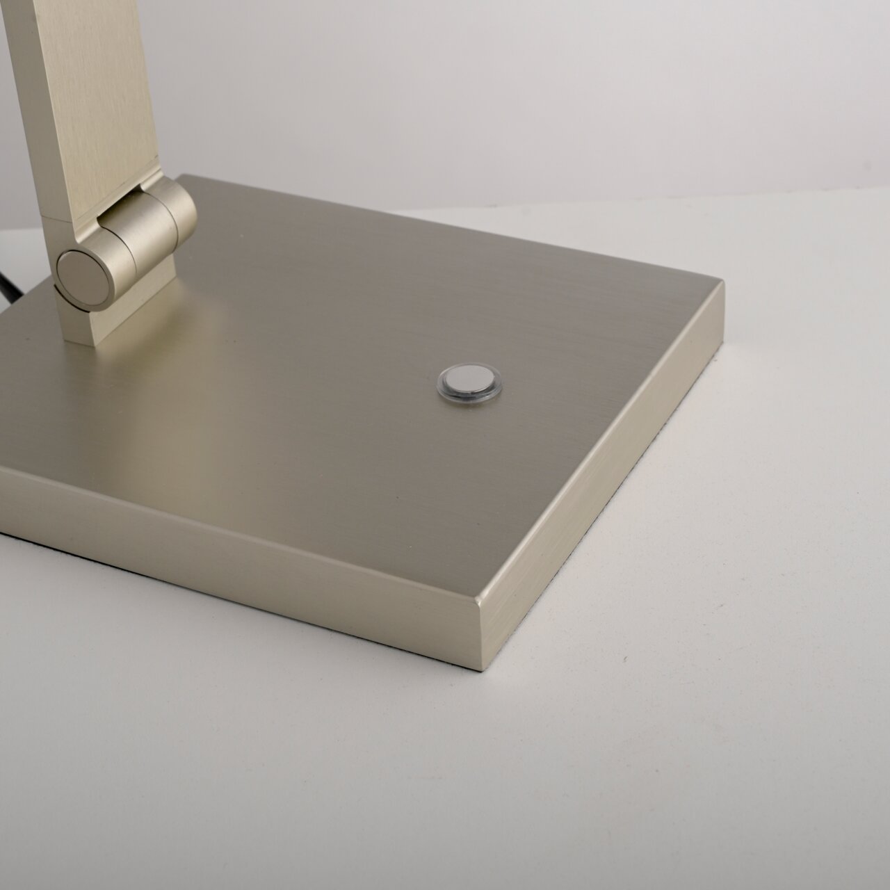 Nahaufnahme der Basis einer LED-Tischleuchte mit modernem, gebürstetem Metallfinish und einem runden Schalter, seitliche Perspektive.