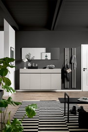 Frontalansicht einer modernen Garderobenkombination mit schwebendem Sideboard in Greige, abgerundetem Wandspiegel und schwarzen Paneel-Kleiderhaken in stilvollem Eingangsbereich.