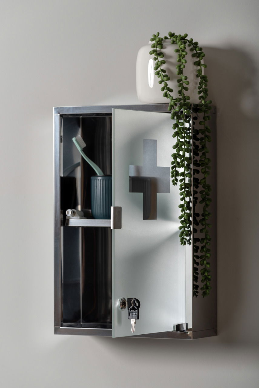 Medizinschrank aus Metall mit Glastür, teilweise geöffnet, mit einem Zahnputzbecher und Zahnbürste im Inneren, dekoriert mit einer Pflanze auf der Oberseite. Perspektive von vorne.