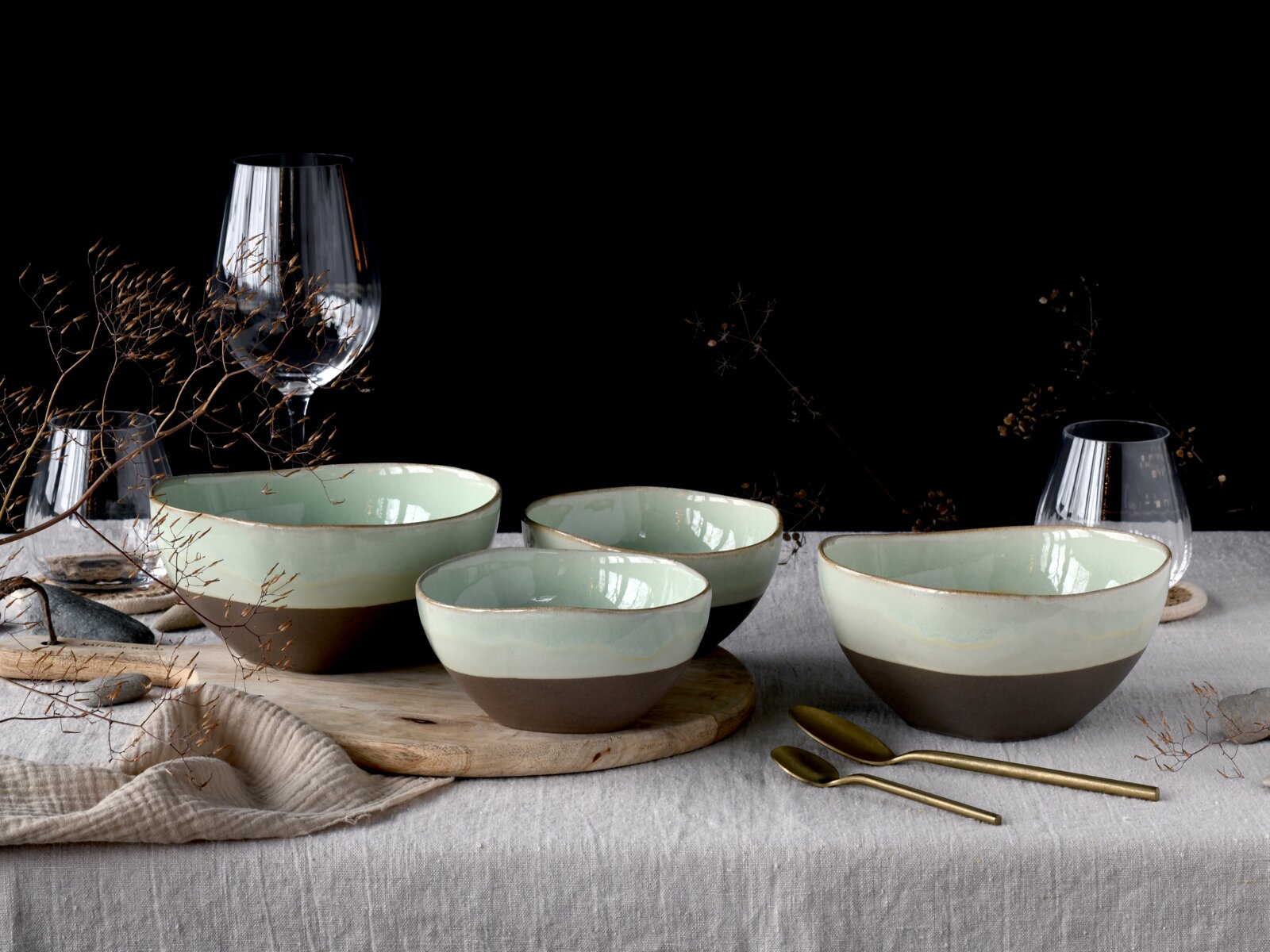 Creatable Bowl 4-tlg BASALT BIO Vier zweifarbige Keramikschalen in Mintgrün und Dunkelbraun auf gedecktem Tisch mit Weingläsern und goldenen Löffeln, frontal in leichter Schrägansicht von vorn fotografiert.