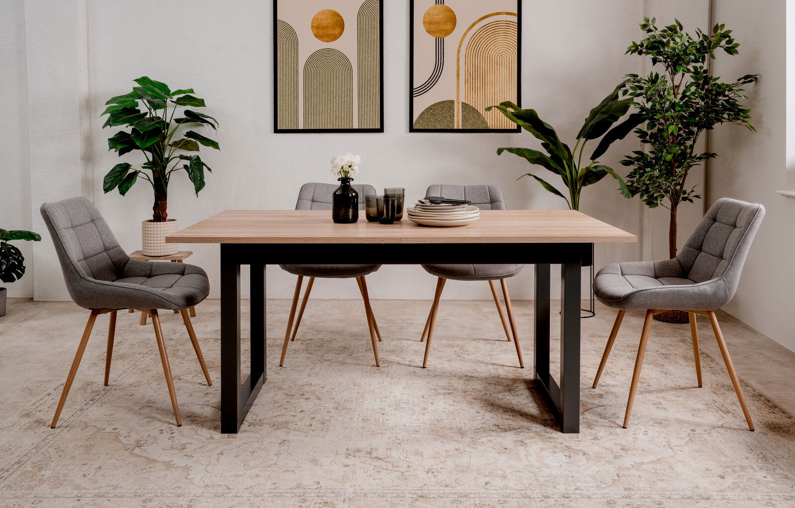 Moderner Esstisch mit Holzplatte und schwarzen Metallbeinen, umgeben von vier grauen Stühlen in einem stilvoll eingerichteten Raum mit Pflanzen und Wandkunst, frontal betrachtet.