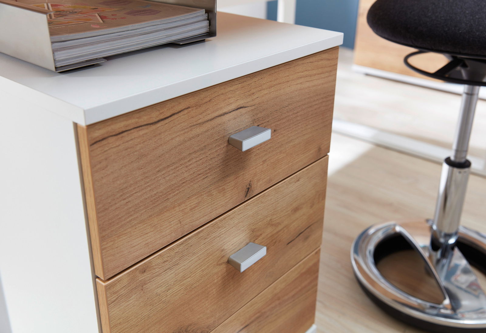 Nahaufnahme eines Rollcontainers mit zwei Holzschubladen und weißen Seiten, von schräg oben fotografiert.