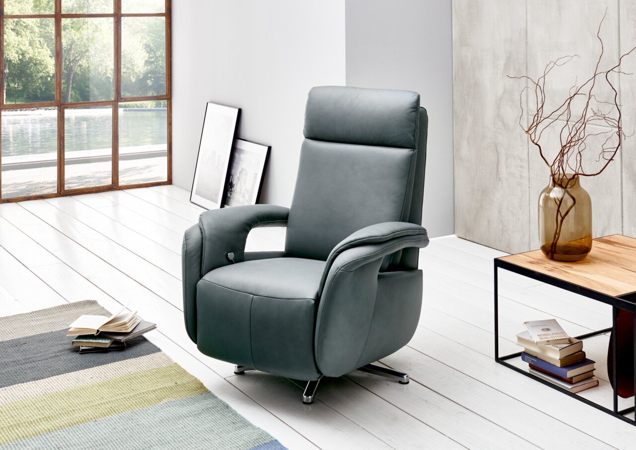 Moderner Relaxsessel in elegantem Grau, seitliche Perspektive, in einem hellen Raum mit großen Fenstern und stilvoller Dekoration.