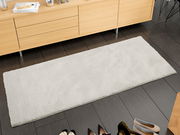 Rechteckiger, cremefarbener Uni-Teppich auf dunklem Holzboden, fotografiert aus der Vogelperspektive, vor einem hellen Holzschrank platziert.