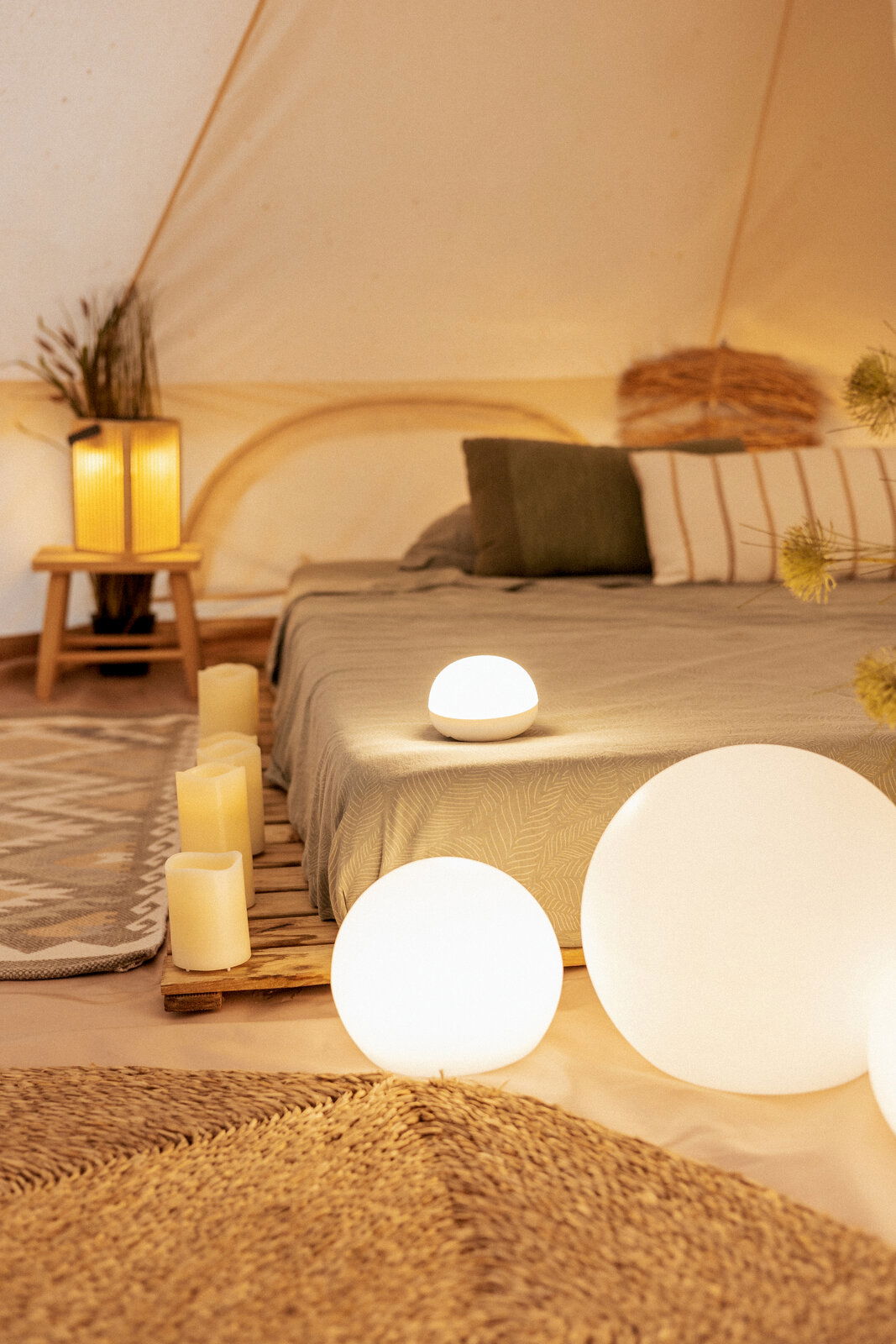Gemütliches Schlafzimmer im Zelt mit leuchtenden, kugelförmigen LED-Lampen am Boden und auf dem Bett, Kerzen und warmem Ambientelicht, aufgenommen aus niedriger Perspektive nahe dem Boden.