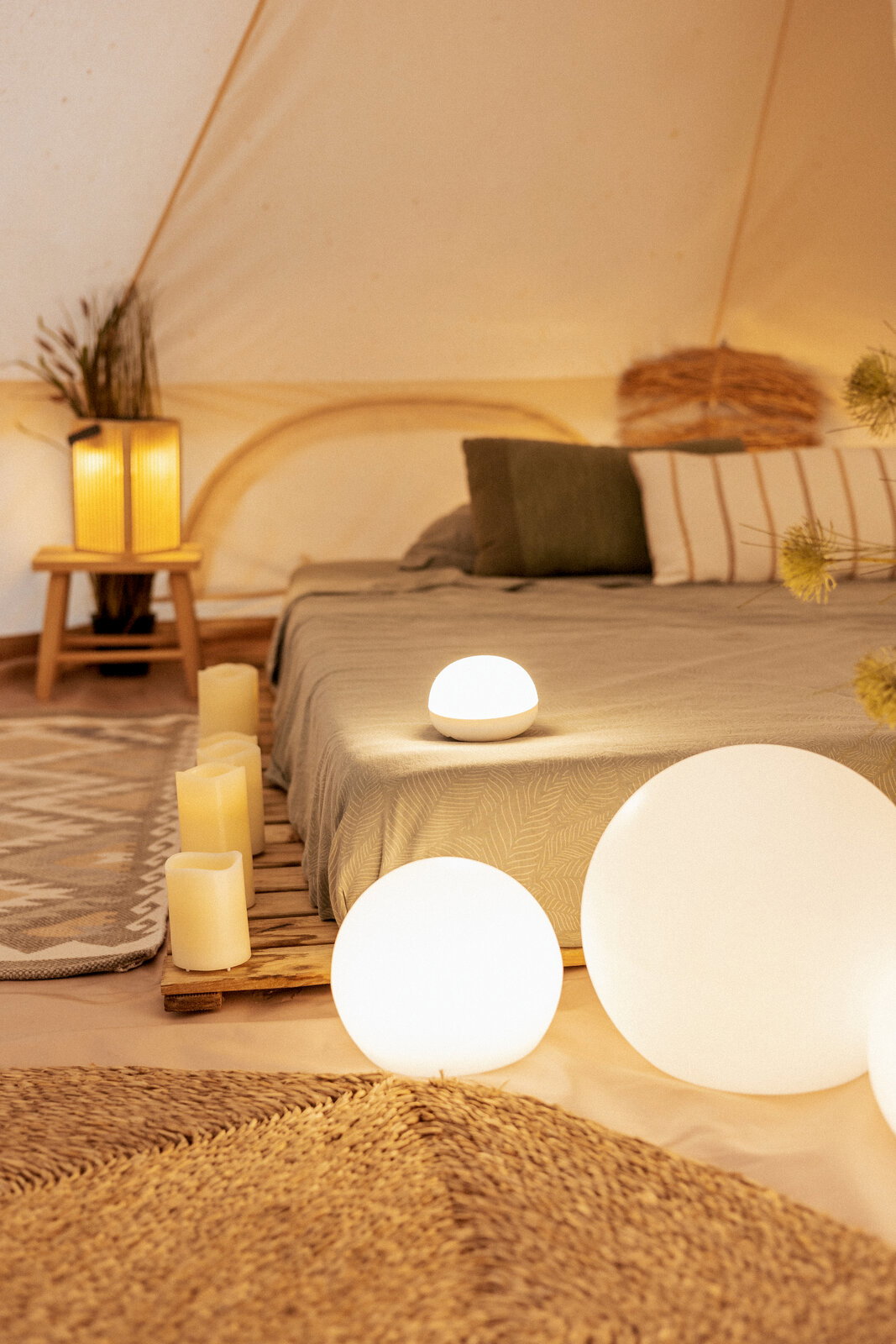 Gemütliches Schlafzimmer im Zelt mit leuchtenden, kugelförmigen LED-Lampen am Boden und auf dem Bett, Kerzen und warmem Ambientelicht, aufgenommen aus niedriger Perspektive nahe dem Boden.