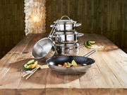 Kochtopfset 5-teilig aus Edelstahl, bestehend aus mehreren Töpfen und einer Pfanne, auf einem Holztisch arrangiert. Perspektive von vorne.