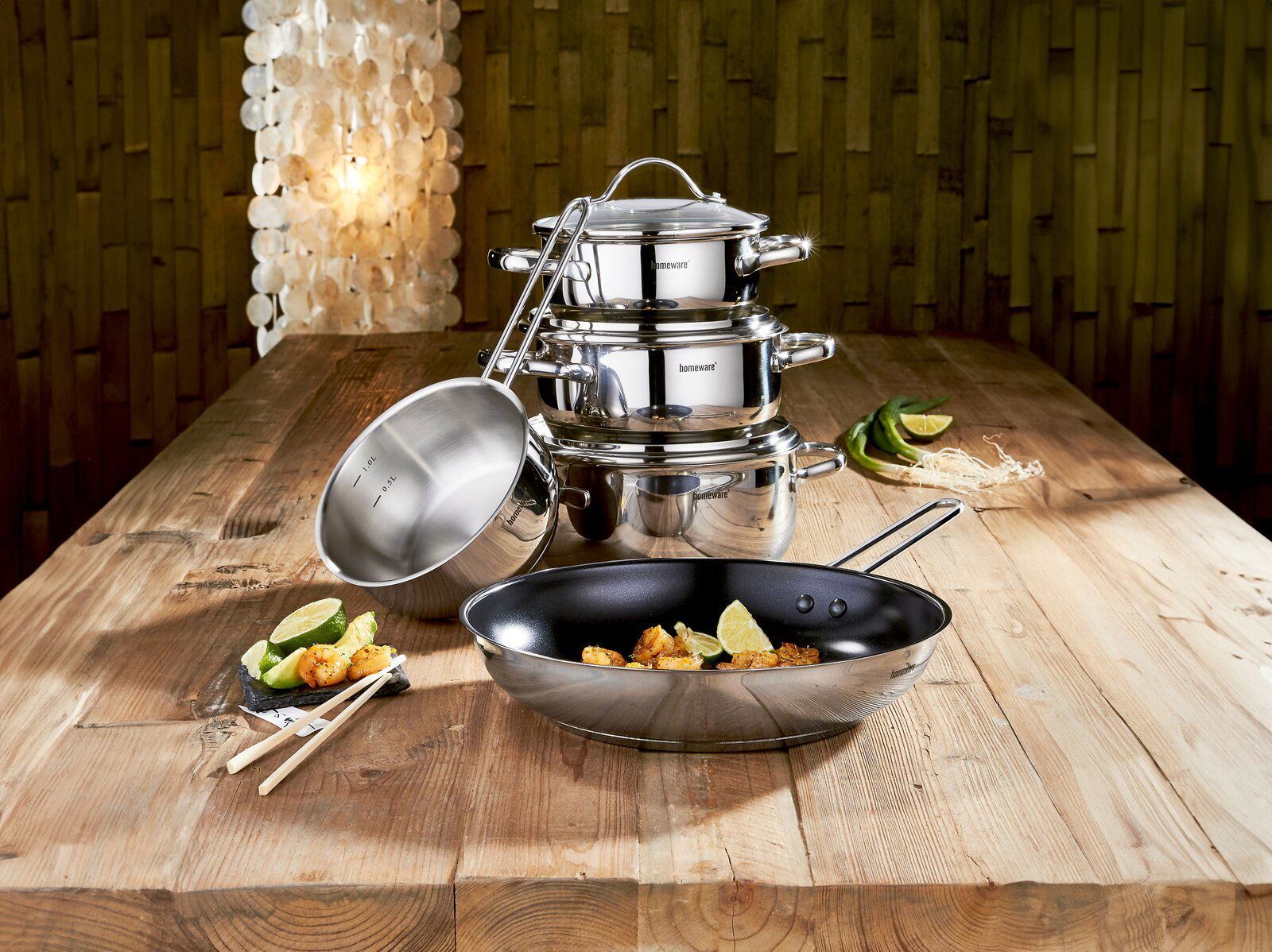 Kochtopfset 5-teilig aus Edelstahl, bestehend aus mehreren Töpfen und einer Pfanne, auf einem Holztisch arrangiert. Perspektive von vorne.