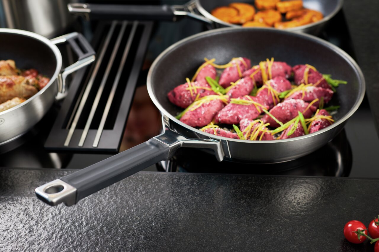 Bratpfanne Silence Pro 32cm mit Griff, gefüllt mit rosa Fleisch und Gemüse, auf einem Herd von schräg oben fotografiert.