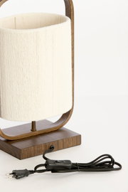 Detailaanzicht van voren van een houten tafellamp met crèmekleurige cilindervormige kap, zwart snoer, schakelaar en Europese stekker